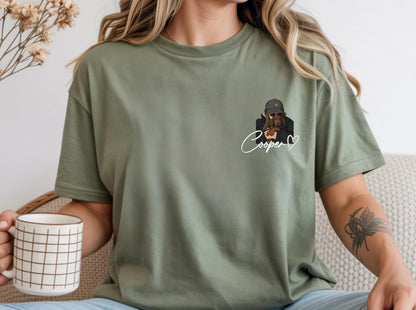 May include: Olive green t-shirt featuring a graphic of a dog wearing a cap and sunglasses, with the name "Cooper" in cursive and a heart. The shirt is a relaxed fit.