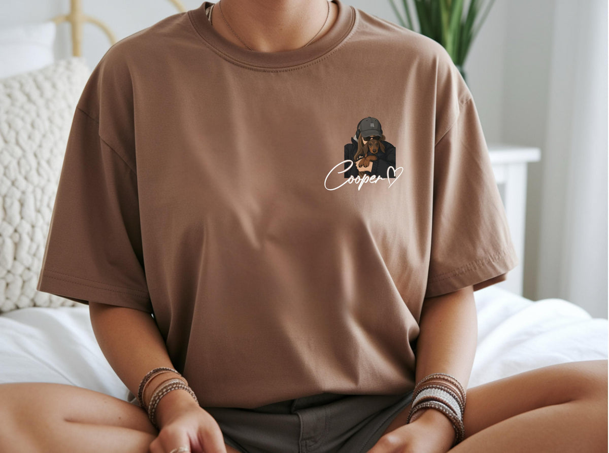 May include: A brown t-shirt with a graphic of a dog wearing a hat and sunglasses, with the name "Cooper" written in cursive below. The shirt is a solid color and has short sleeves.