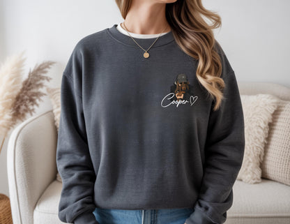 May include: Dark gray sweatshirt with a crew neck. The sweatshirt features a small graphic of a dog wearing a hat and sunglasses, with the name "Cooper" written in cursive below the graphic, along with a heart symbol.