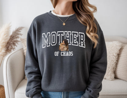 May include: Dark gray sweatshirt with the words "MOTHER of CHAOS" in white block letters. A graphic of a woman holding a child is centered below the word "MOTHER". The sweatshirt has a crew neck and long sleeves.