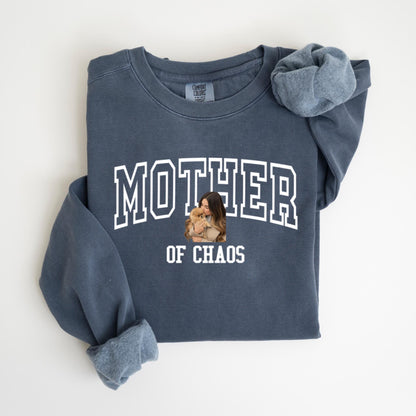 May include: A navy blue sweatshirt with the words "MOTHER" and "OF CHAOS" in white block letters. A photo of a woman holding a small dog is in the center. The sweatshirt has long sleeves and a crew neck.