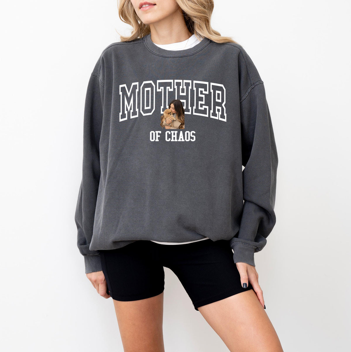 May include: A charcoal gray sweatshirt with the words "MOTHER" in white block letters above "OF CHAOS". A small image of a person holding a dog is centered below the word "MOTHER". The sweatshirt is worn with black shorts and a white undershirt.
