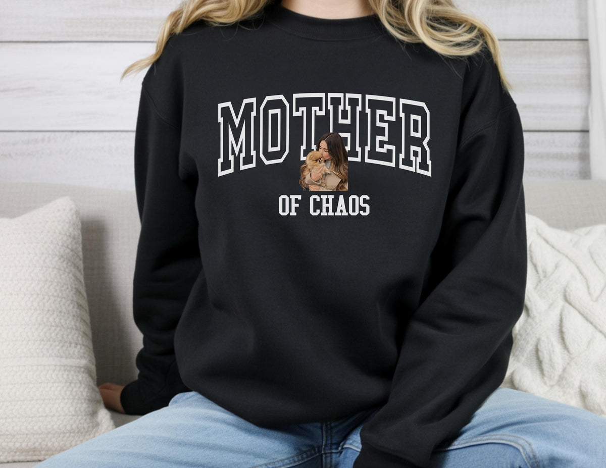 May include: Black sweatshirt with the words "MOTHER" above "OF CHAOS" in white block letters. A photo of a person holding a child is in the center. The sweatshirt is a crew neck style.