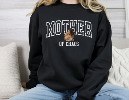 May include: Black sweatshirt with the words "MOTHER" above "OF CHAOS" in white block letters. A photo of a person holding a child is in the center. The sweatshirt is a crew neck style.