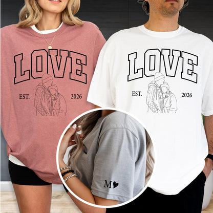 May include: A pair of matching shirts, one dusty rose and one white, featuring the word "LOVE" in bold black letters. Below the word is a line drawing of a couple and the text "EST. 2026". The sleeve of one shirt has the letter "M" and a heart.