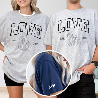 May include: Two gray sweatshirts with the word "LOVE" in black block letters. Below the word "LOVE" is the text "EST. 2026" and a line drawing of two people. A close-up shows a blue sleeve with the letter "M" and a heart.