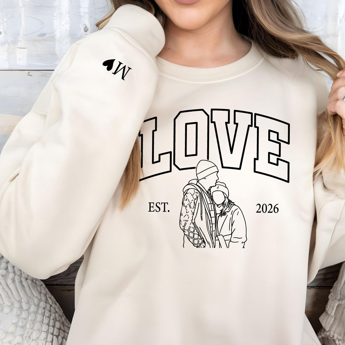 May include: Cream-colored sweatshirt with the word "LOVE" in large, black, block letters. Below the word "LOVE" is a black and white line drawing of a couple. The text "EST. 2026" is below the drawing. A black heart and the letter "W" are on the left sleeve.