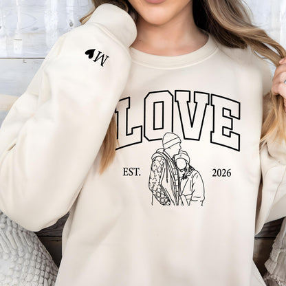 May include: Cream-colored sweatshirt with the word "LOVE" in large, black, block letters. Below the word "LOVE" is a black and white line drawing of a couple. The text "EST. 2026" is below the drawing. A black heart and the letter "W" are on the left sleeve.