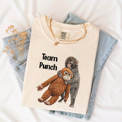 May include: Cream-colored t-shirt with the text "Team Punch" and a graphic of two monkeys embracing. One monkey is brown, the other is gray. A gold necklace is draped across the shirt.