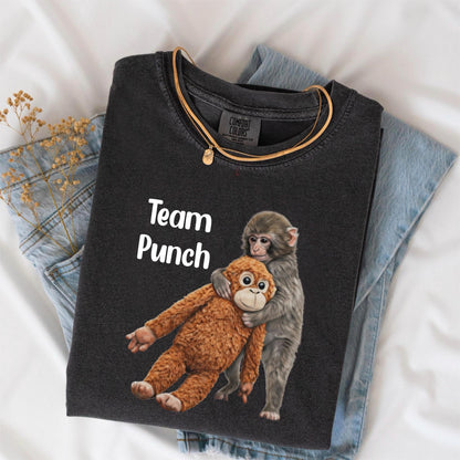 May include: Dark gray t-shirt with the text "Team Punch" and a graphic of two monkeys hugging. One monkey is brown, the other is gray. A gold necklace is draped over the shirt, which is folded on top of blue jeans.