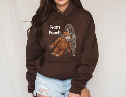 May include: A dark brown hoodie with the text "Team Punch" above a graphic of two monkeys embracing. One monkey is brown, and the other is gray. The hoodie has a drawstring and a front pocket.
