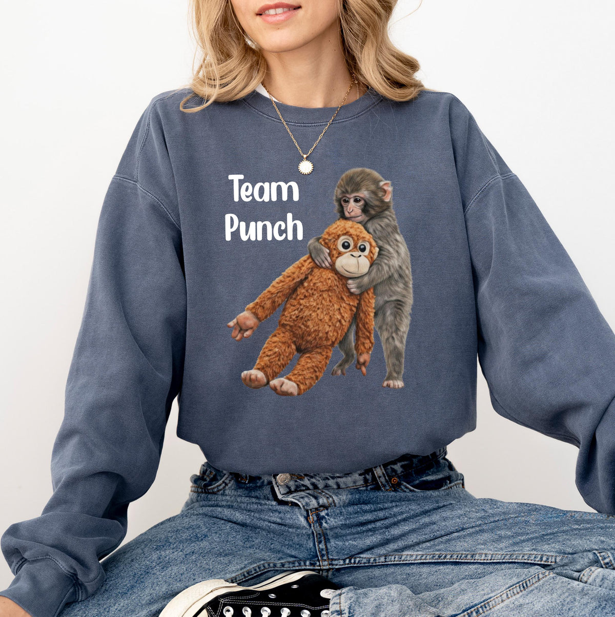 May include: A blue-grey sweatshirt with the text "Team Punch" in white. The graphic features two monkeys, one hugging the other. The hugging monkey is grey, and the other is brown. The sweatshirt is a casual style.