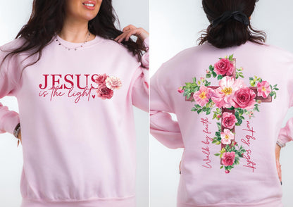 May include: A light pink sweatshirt with the text "JESUS is the light" and a floral design. The back features a cross adorned with pink roses and the text "Walk by faith, not by sight."