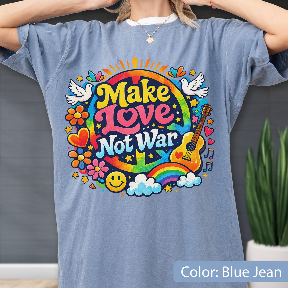 May include: Blue jean colored t-shirt with a colorful graphic that says "Make Love Not War". The graphic includes a rainbow, guitar, doves, flowers, and a smiley face. The shirt is a relaxed fit.