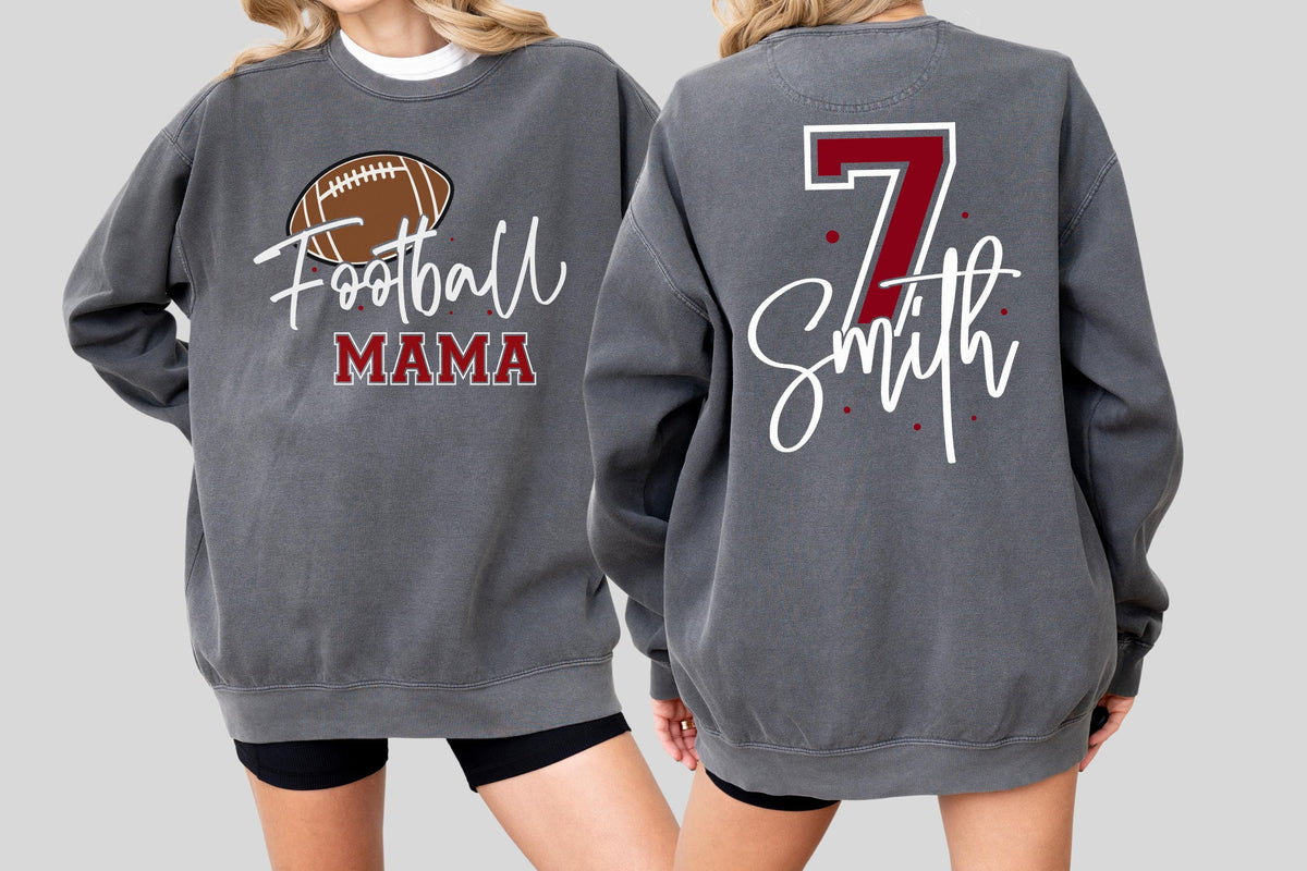 May include: A charcoal gray crewneck sweatshirt featuring a brown football graphic with the text Football MAMA on the front, and the number 7 in red with the name Smith in white script lettering on the back, accented by small red dots.