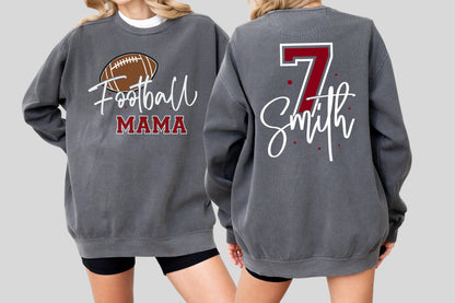 May include: A charcoal gray crewneck sweatshirt featuring a brown football graphic with the text Football MAMA on the front, and the number 7 in red with the name Smith in white script lettering on the back, accented by small red dots.