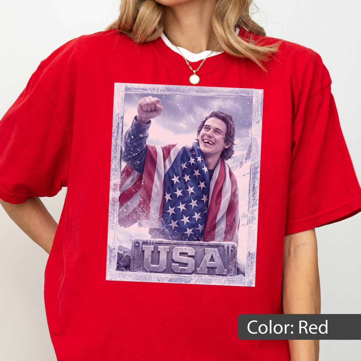 May include: A red t-shirt featuring a framed image of a person wrapped in an American flag, with the word "USA" at the bottom. The person is smiling and has their fist raised. The shirt is a solid red color.