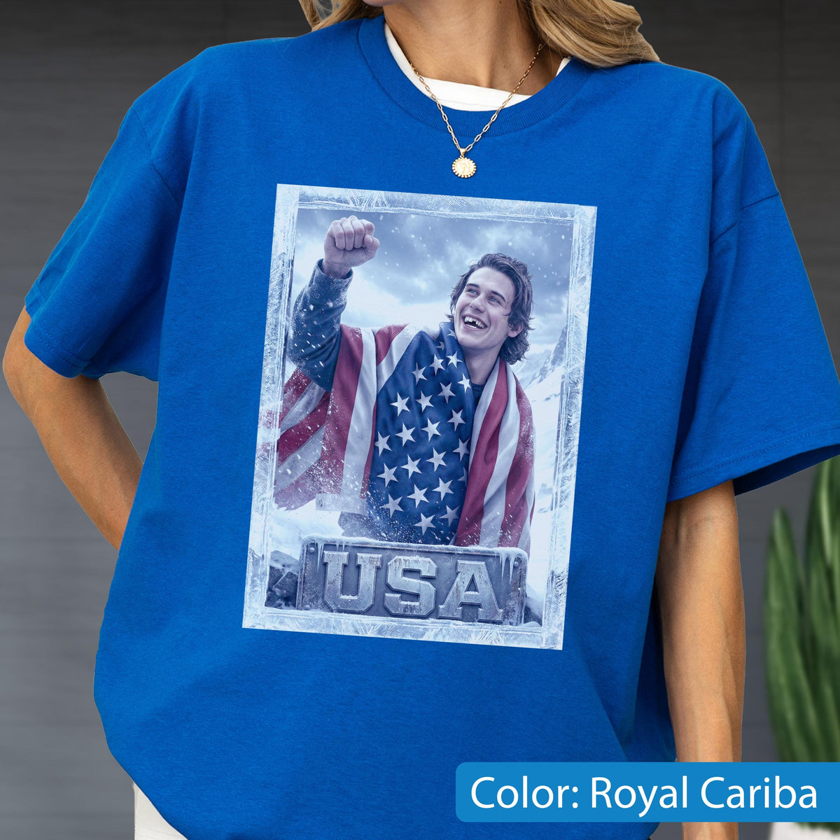 May include: Royal Cariba blue t-shirt featuring a framed image of a person wrapped in an American flag. The image has the word "USA" at the bottom. The person in the image is smiling and has their fist raised.