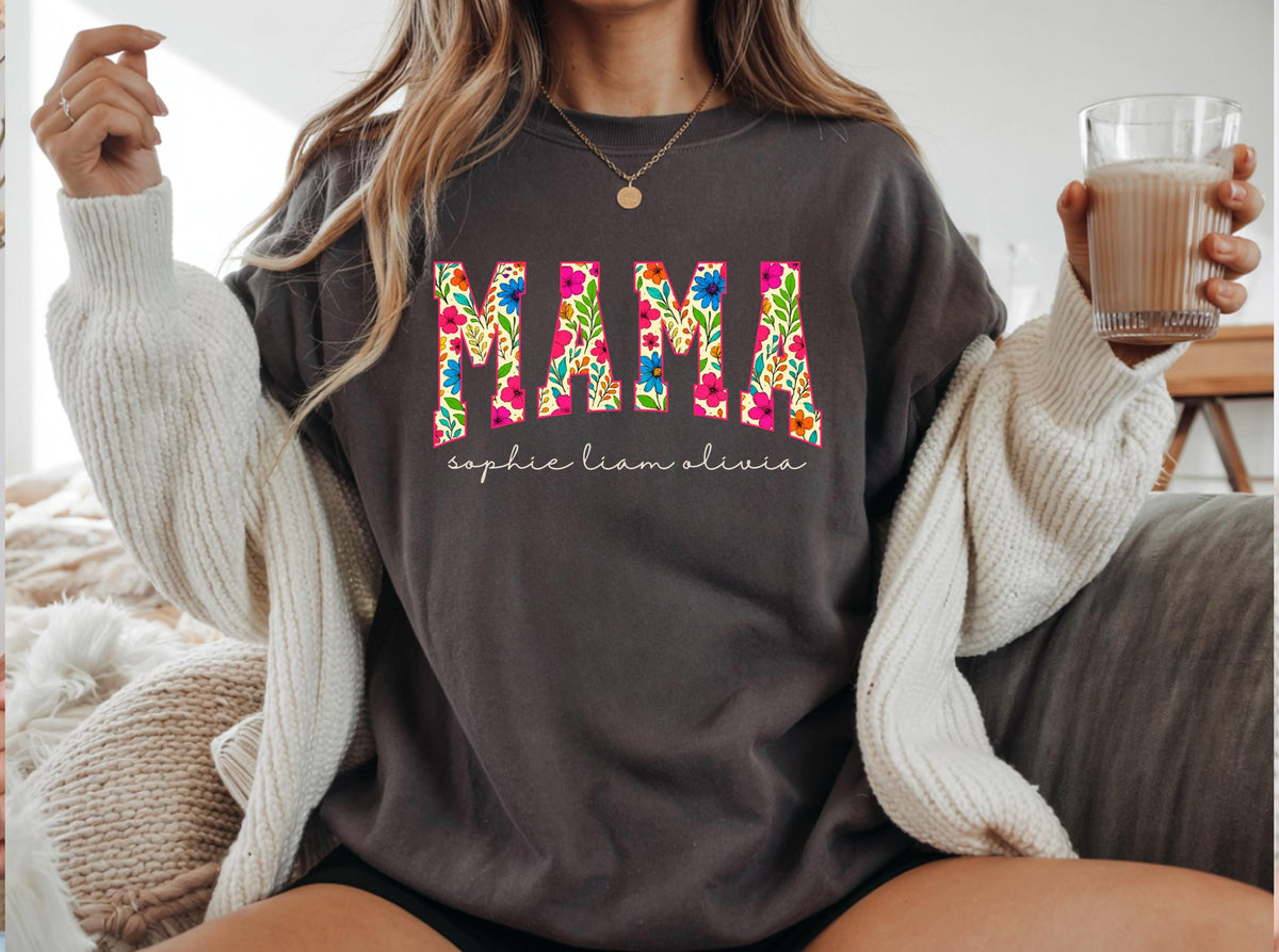 May include: Dark gray sweatshirt with the word "MAMA" in colorful floral letters. Below the word "MAMA" are the names "sophie liam olivia" in a script font. The sweatshirt is a casual style.