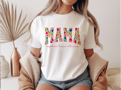 May include: White t-shirt with the word "MAMA" in large, floral-patterned letters. Below the word "MAMA" are the names "sophie liam olivia" in a cursive font. The shirt is worn by a person.