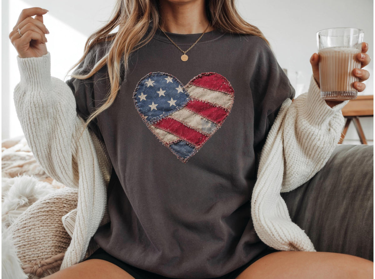 May include: Dark gray sweatshirt featuring a heart-shaped design resembling the American flag. The heart is made of patches with red and white stripes and a blue field with white stars. The sweatshirt is a casual style.