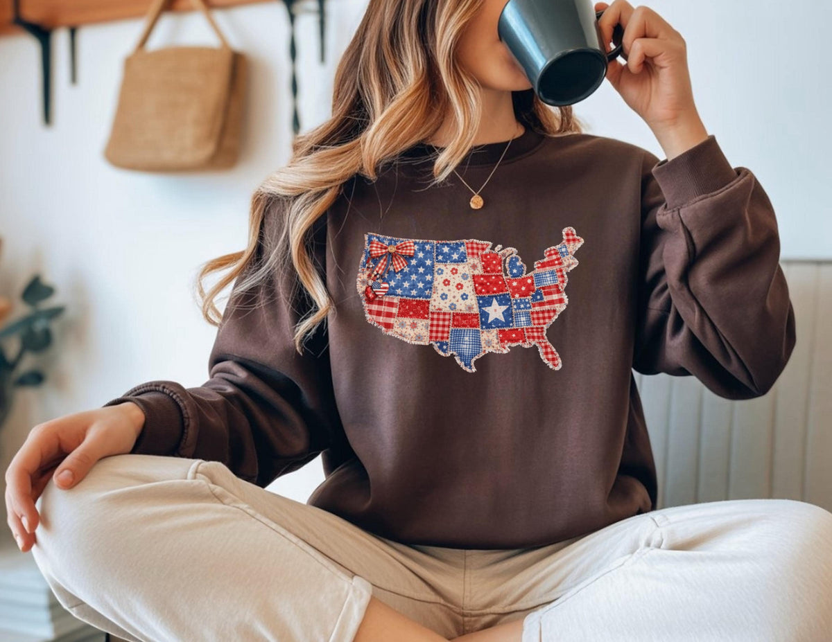 May include: A brown sweatshirt featuring a patchwork design of the United States map in red, white, and blue. The design incorporates stars, stripes, and various patterns. The sweatshirt has a crew neck and long sleeves.