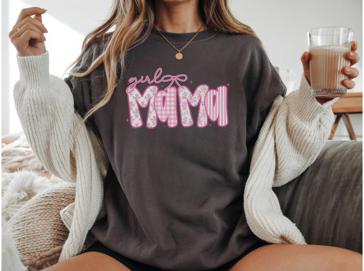 May include: Dark gray sweatshirt with the text "girl MAMA" in pink and white. The word "MAMA" has a pink outline and is filled with a floral, gingham, and striped pattern. A white cardigan is draped over the shoulders.