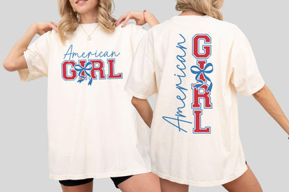 May include: Cream-colored t-shirt with the text "American Girl" in blue script and red block letters, accented with a blue bow. The back of the shirt repeats the design vertically. A casual, patriotic style.
