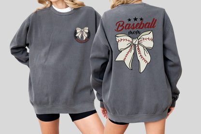 May include: A charcoal gray sweatshirt with a white crew neck peeking out. The front features a bow design within a circular emblem. The back displays the words "Baseball mom" above a large bow design with baseball stitching.
