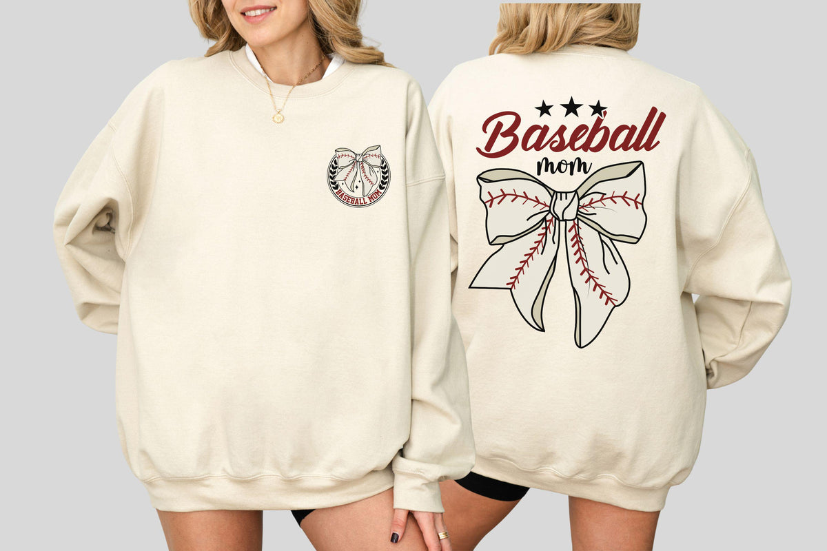 May include: Cream-colored sweatshirt with a baseball-themed design. The front features a bow and the words "Baseball Mom" on the back. The design incorporates baseball stitching and stars.