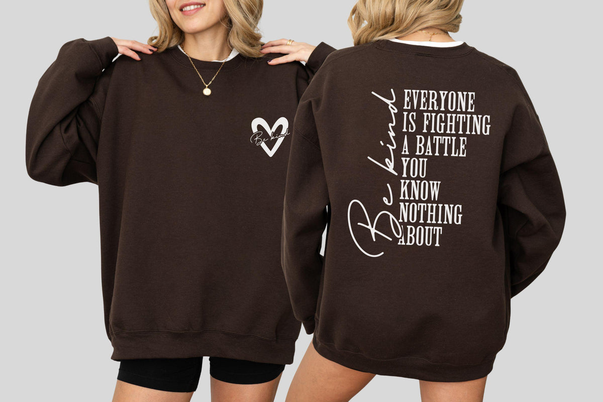 May include: A brown sweatshirt with a white heart design on the front and the words "Be Kind" and "Everyone is fighting a battle you know nothing about" printed on the back. The sweatshirt has a crew neck.
