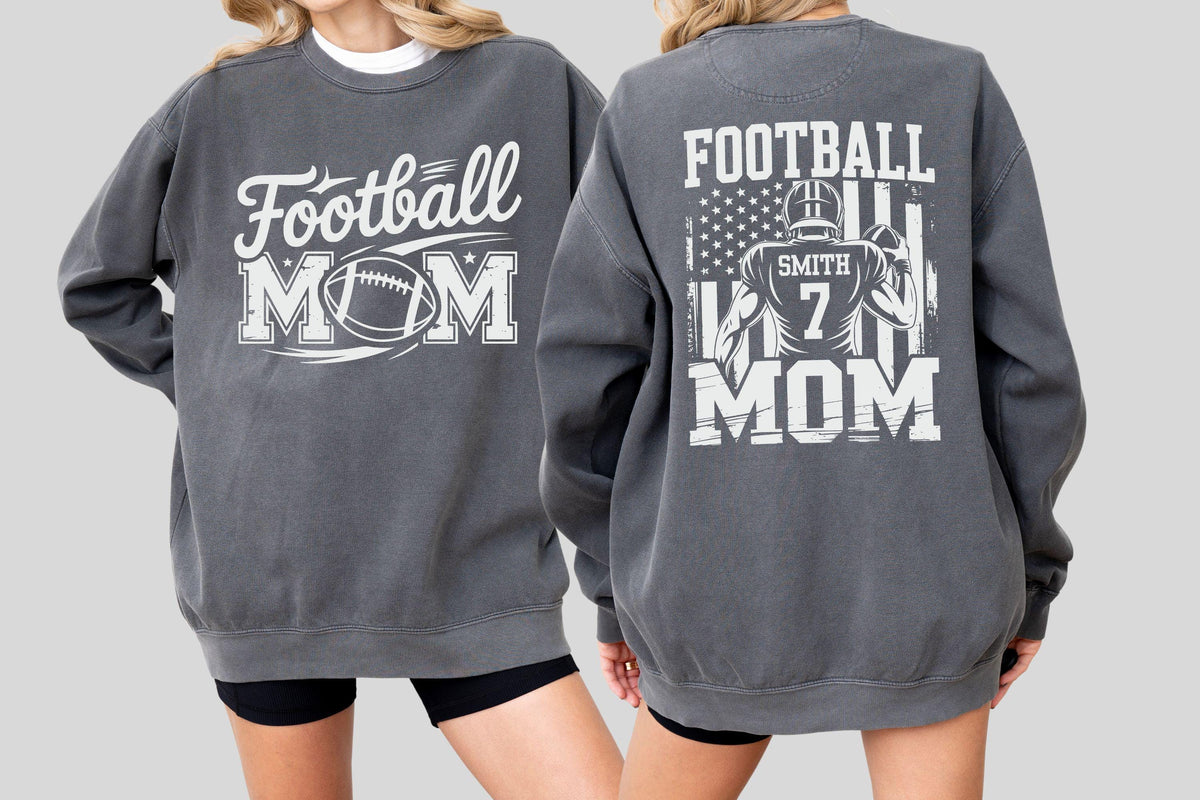 May include: Charcoal gray sweatshirt with white text and graphics. The front reads "Football MOM" with a football graphic. The back features a football player graphic, the text "FOOTBALL MOM", and an American flag design.