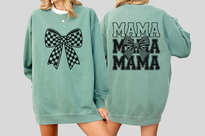 May include: A sage green sweatshirt featuring a large black and white checkered bow on the front. The back of the sweatshirt displays the word "MAMA" three times, with a checkered bow in the middle.