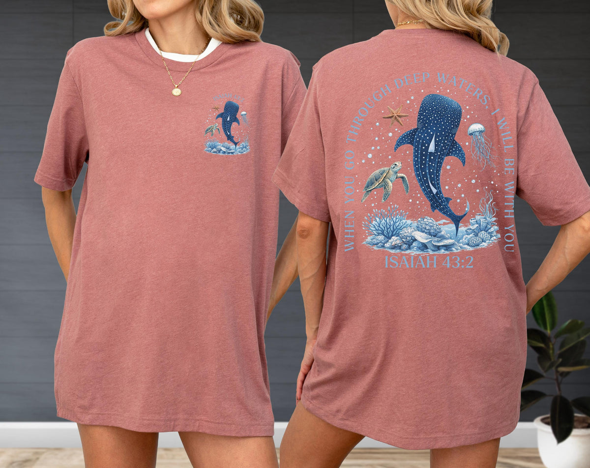 May include: A dusty rose t-shirt with a white collar. The front features a small graphic of a whale shark and ocean elements. The back displays a larger design with a whale shark, turtle, jellyfish, and text that reads "WHEN YOU GO THROUGH DEEP WATERS, I WILL BE WITH YOU. ISAIAH 43:2."
