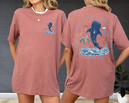 May include: A dusty rose t-shirt with a white collar. The front features a small graphic of a whale shark and ocean elements. The back displays a larger design with a whale shark, turtle, jellyfish, and text that reads "WHEN YOU GO THROUGH DEEP WATERS, I WILL BE WITH YOU. ISAIAH 43:2."