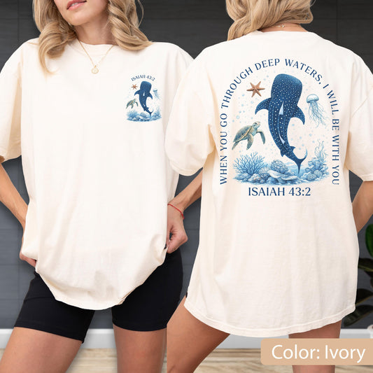 May include: Ivory-colored t-shirt featuring a blue whale and sea life graphic. The front has a small design with text "ISAIAH 43:2". The back displays a larger design with the text "WHEN YOU GO THROUGH DEEP WATERS, I WILL BE WITH YOU" and "ISAIAH 43:2".