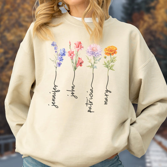 May include: Beige sweatshirt featuring a floral design with the names "Jennifer", "John", "Patricia", and "Mary" in a script font. The flowers are in shades of purple, pink, and orange.
