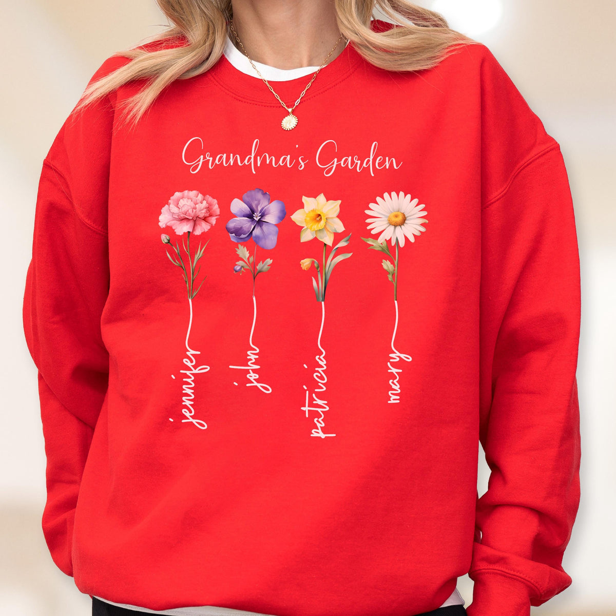 May include: A red sweatshirt featuring the text "Grandma's Garden" above four floral illustrations. Each flower has a name written below it: Jennifer, John, Patricia, and Mary. The flowers are pink, purple, yellow, and white.