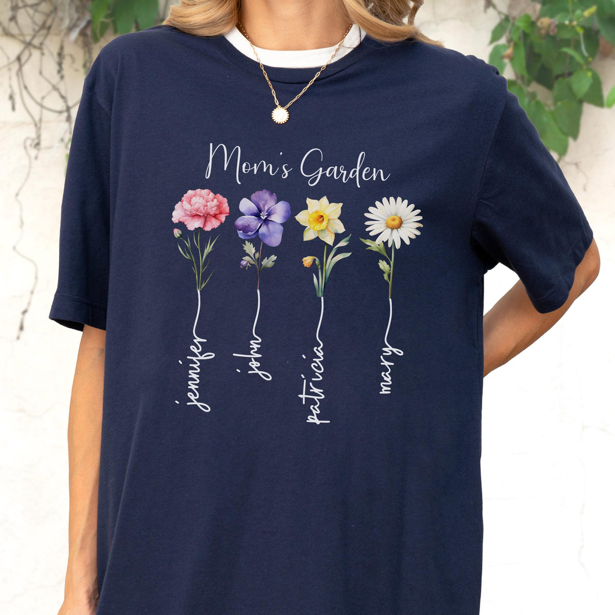 May include: Navy blue t-shirt with a white collar featuring the text "Mom's Garden" above four colorful flower illustrations. Each flower has a name written below it: Jennifer, John, Patricia, and Mary.