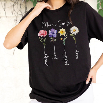 May include: Black t-shirt featuring the text "Mom's Garden" above four colorful flower illustrations. Each flower has a name written below it: Jennifer, John, Patricia, and Mary. The flowers are pink, purple, yellow, and white.