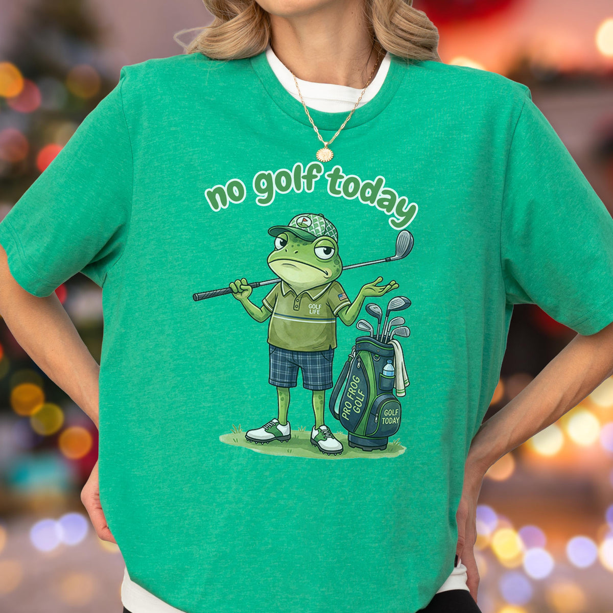 May include: Green t-shirt with the text "no golf today." The shirt features a cartoon frog wearing a golf hat and holding a golf club. A golf bag with clubs is next to the frog. The frog is wearing a green polo shirt and blue plaid shorts.