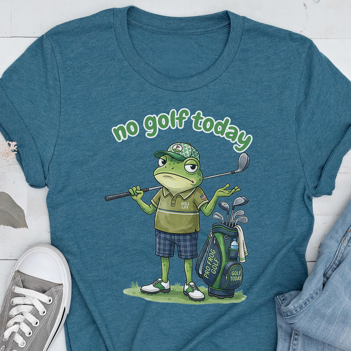 May include: Teal t-shirt featuring a cartoon frog with a golf club and golf bag. The frog is wearing a golf hat, polo shirt, and plaid shorts. Text on the shirt reads "no golf today". The golf bag has the text "Pro Frog Golf" and "Golf Today".