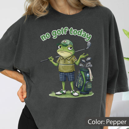 May include: Pepper-colored t-shirt featuring a cartoon frog golfer with the text "no golf today." The frog is wearing a golf hat, polo shirt, and plaid shorts, holding a golf club. A golf bag with clubs is beside him.