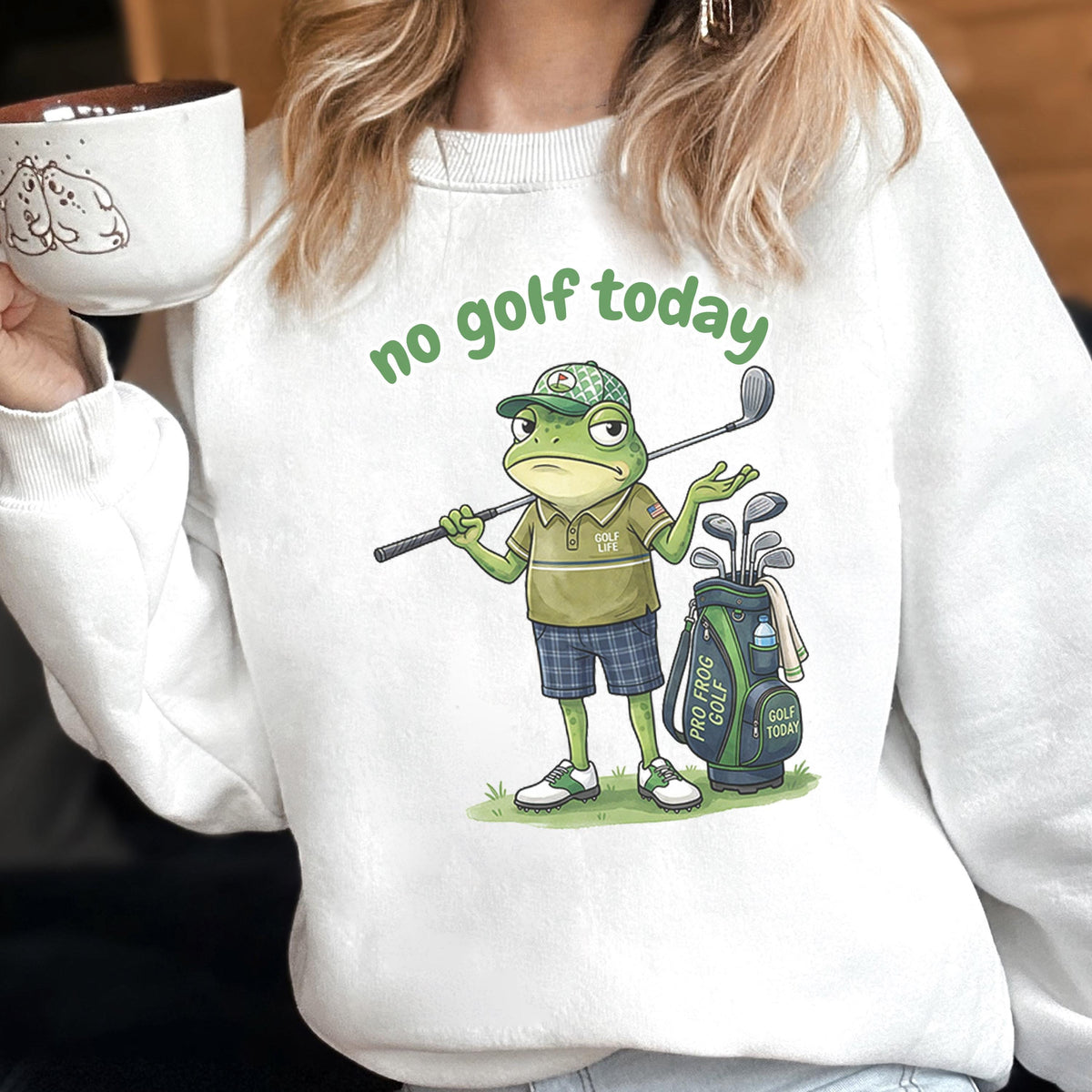 May include: White sweatshirt with the phrase "no golf today" in green. The graphic features a grumpy frog wearing a golf cap and holding a golf club. A golf bag with clubs is next to the frog.