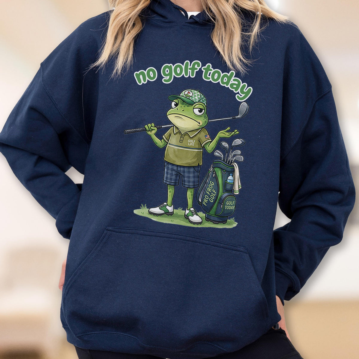 May include: Navy blue hoodie featuring a cartoon frog golfer with the text "no golf today". The frog is wearing a golf cap, polo shirt, and plaid shorts, holding a golf club. A golf bag with clubs is next to the frog.