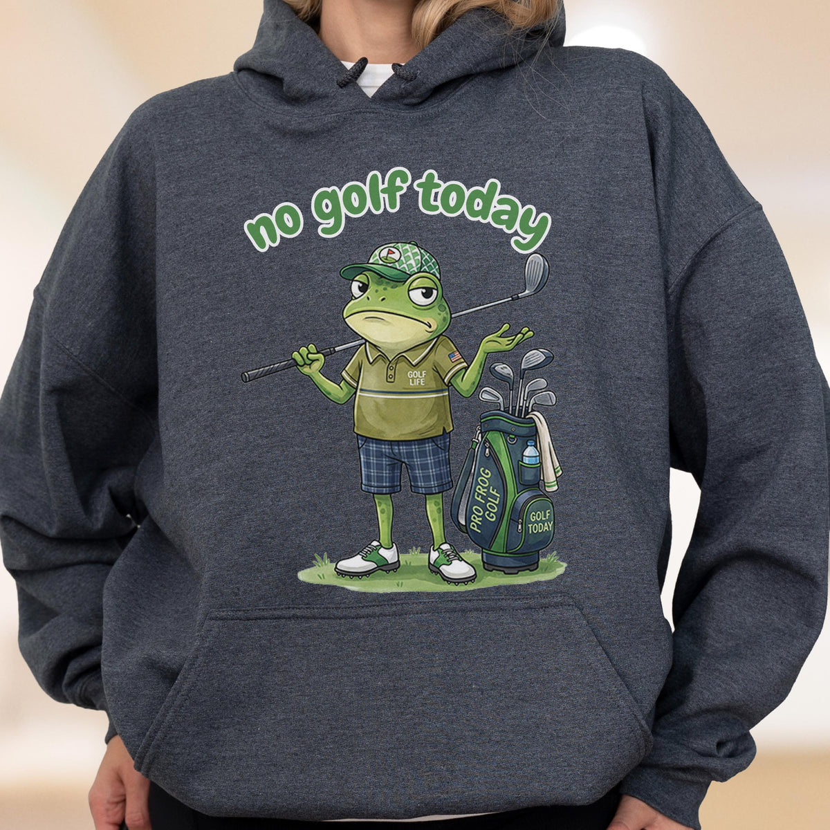 May include: Dark gray hoodie featuring a cartoon frog golfer with the text "no golf today." The frog is wearing a golf hat, polo shirt, and shorts, holding a golf club. A golf bag with "Pro Frog Golf" is next to him.