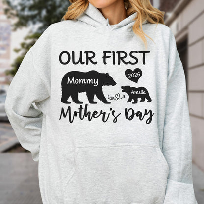 May include: A light gray hoodie with a black graphic that reads "OUR FIRST Mother's Day" with bear silhouettes. The design includes the words "Mommy" and "Amelia" with the year "2026" in a heart.