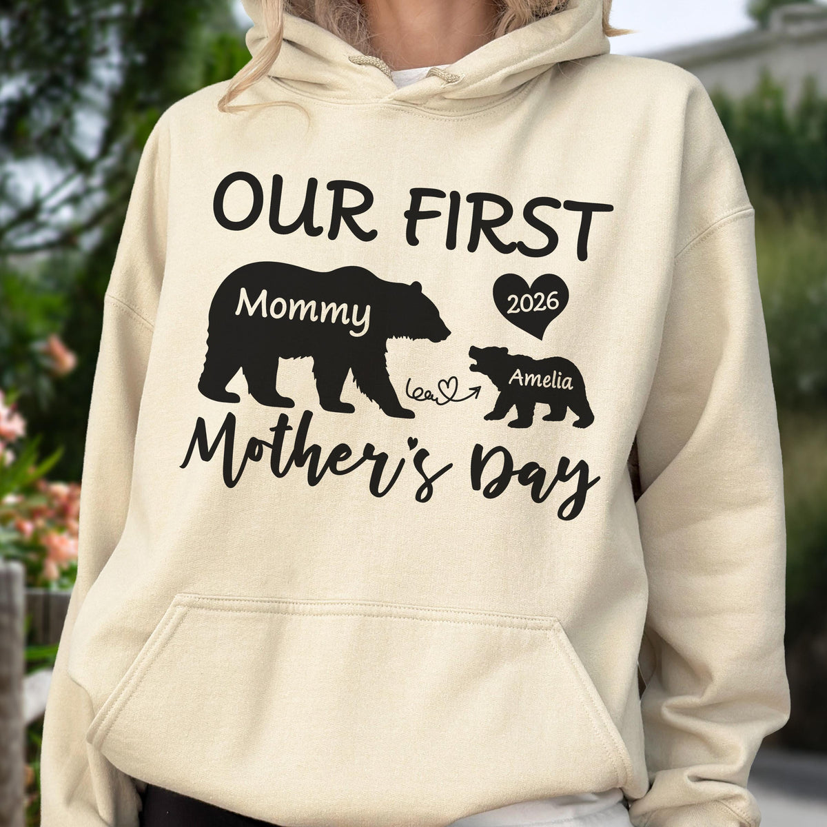 May include: A beige hoodie with a black graphic that reads "OUR FIRST Mother's Day" with bear silhouettes. The larger bear says "Mommy" and the smaller bear says "Amelia" with a heart and the year 2026.