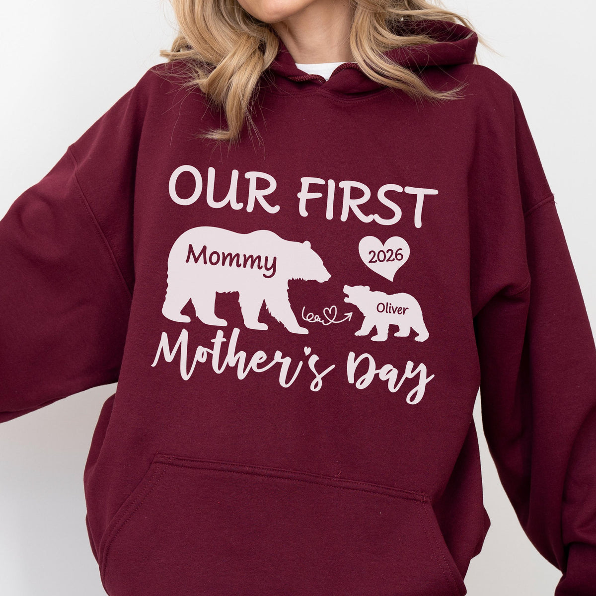 May include: A maroon hoodie with white text and graphics. The text reads "OUR FIRST Mother's Day" with a bear graphic labeled "Mommy" and a smaller bear labeled "Oliver" with a heart and the year "2026".