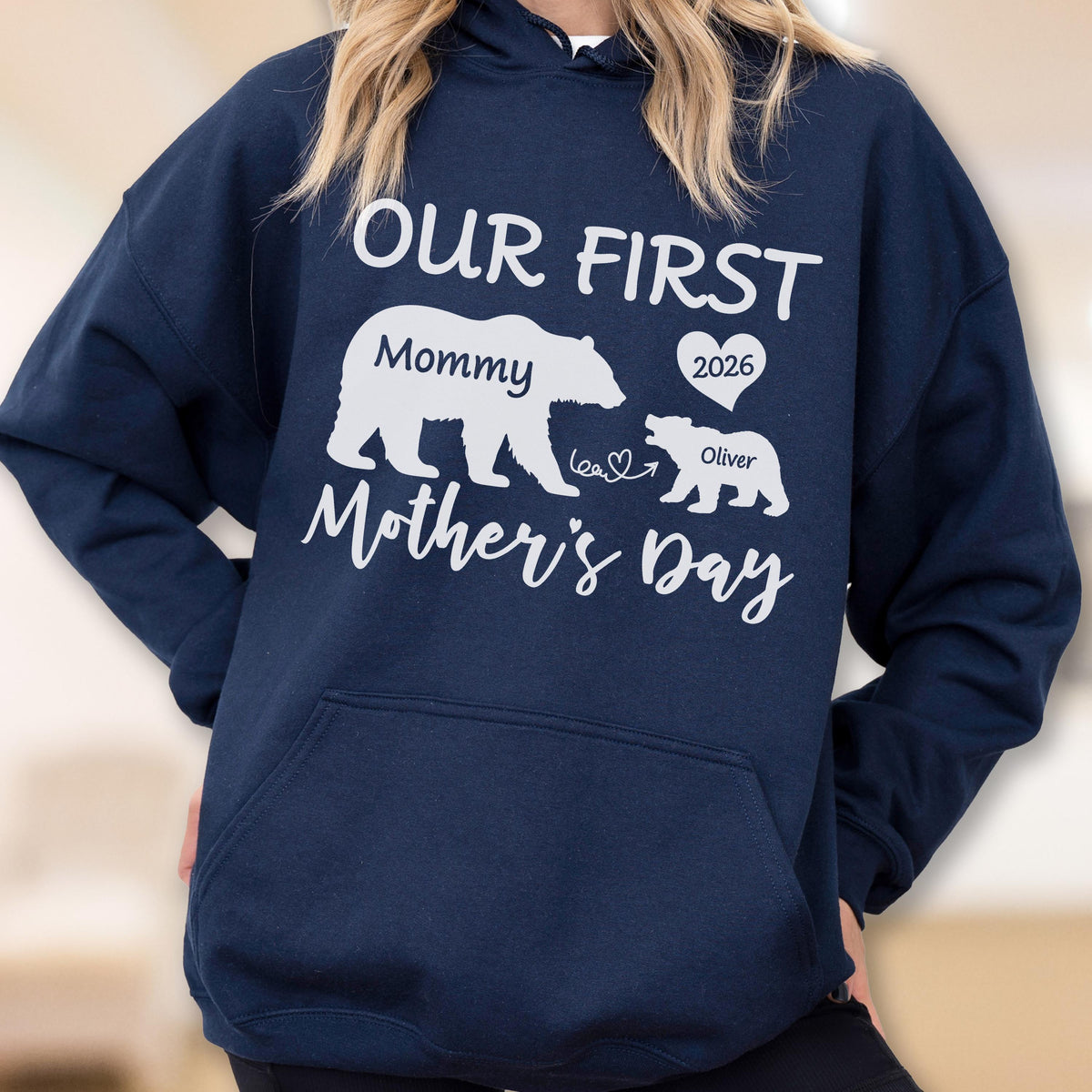 May include: Navy blue hooded sweatshirt with white text and graphics. The design includes the words "OUR FIRST Mother's Day" and bear illustrations. The word "Mommy" is above a larger bear, and "Oliver" is above a smaller bear, with the year "2026" in a heart.